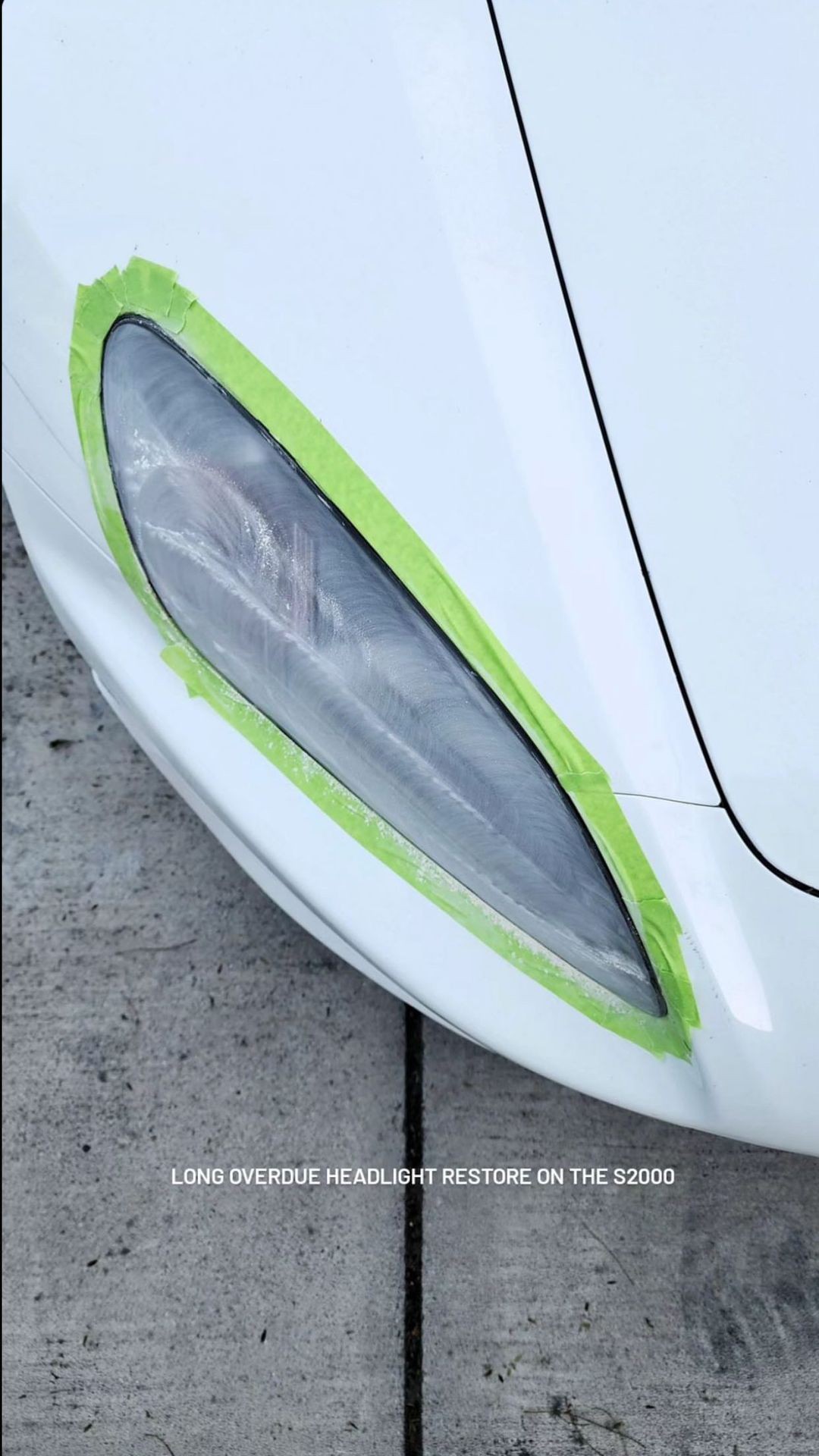 Car headlight masked with green tape for restoration on a white vehicle.