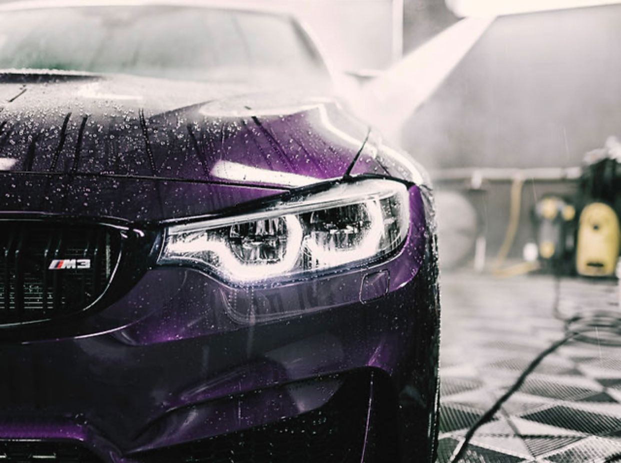 Close-up of a purple sports car with rain droplets on its hood in a garage setting.