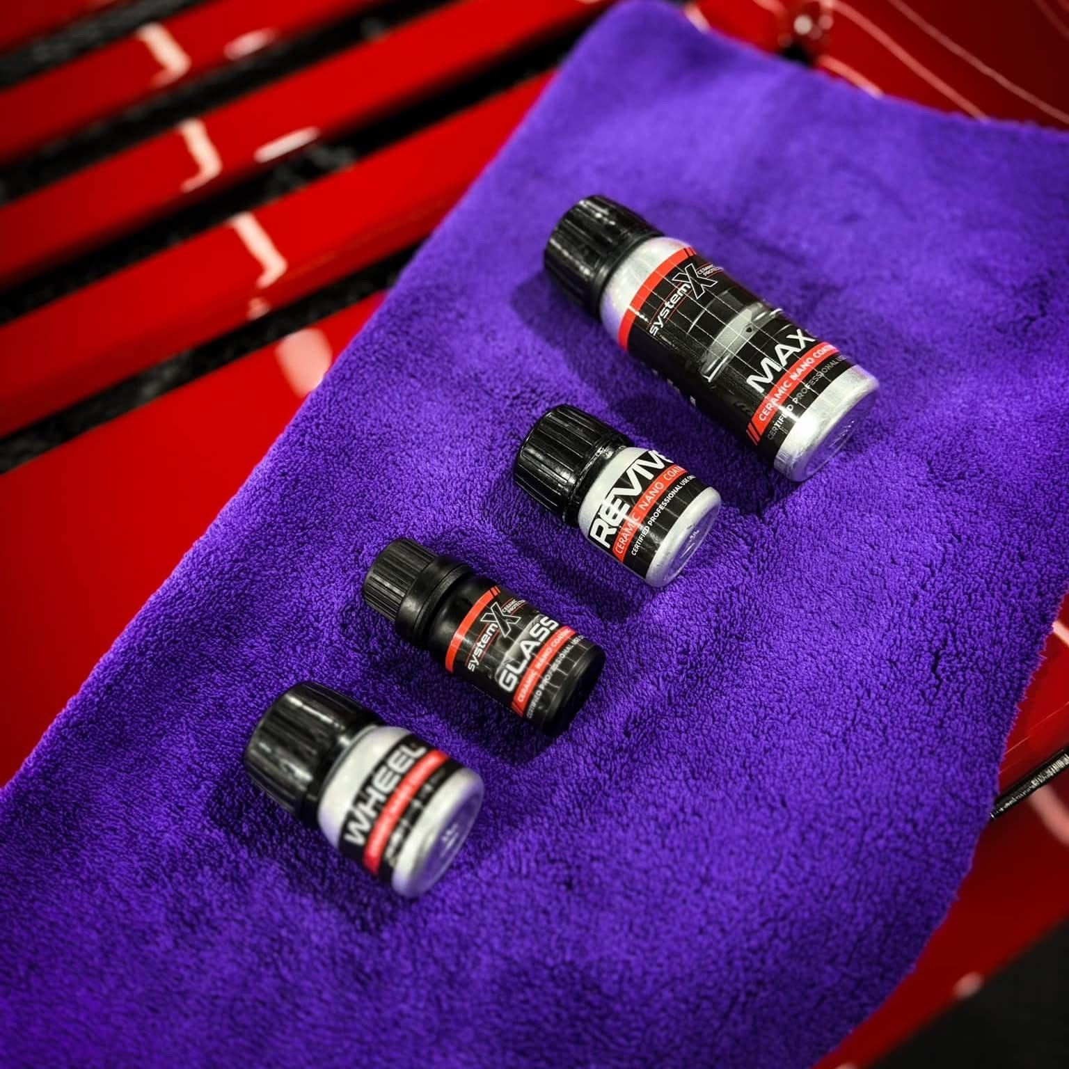 Four small bottles of car detailing products placed on a purple microfiber towel, with a red background.