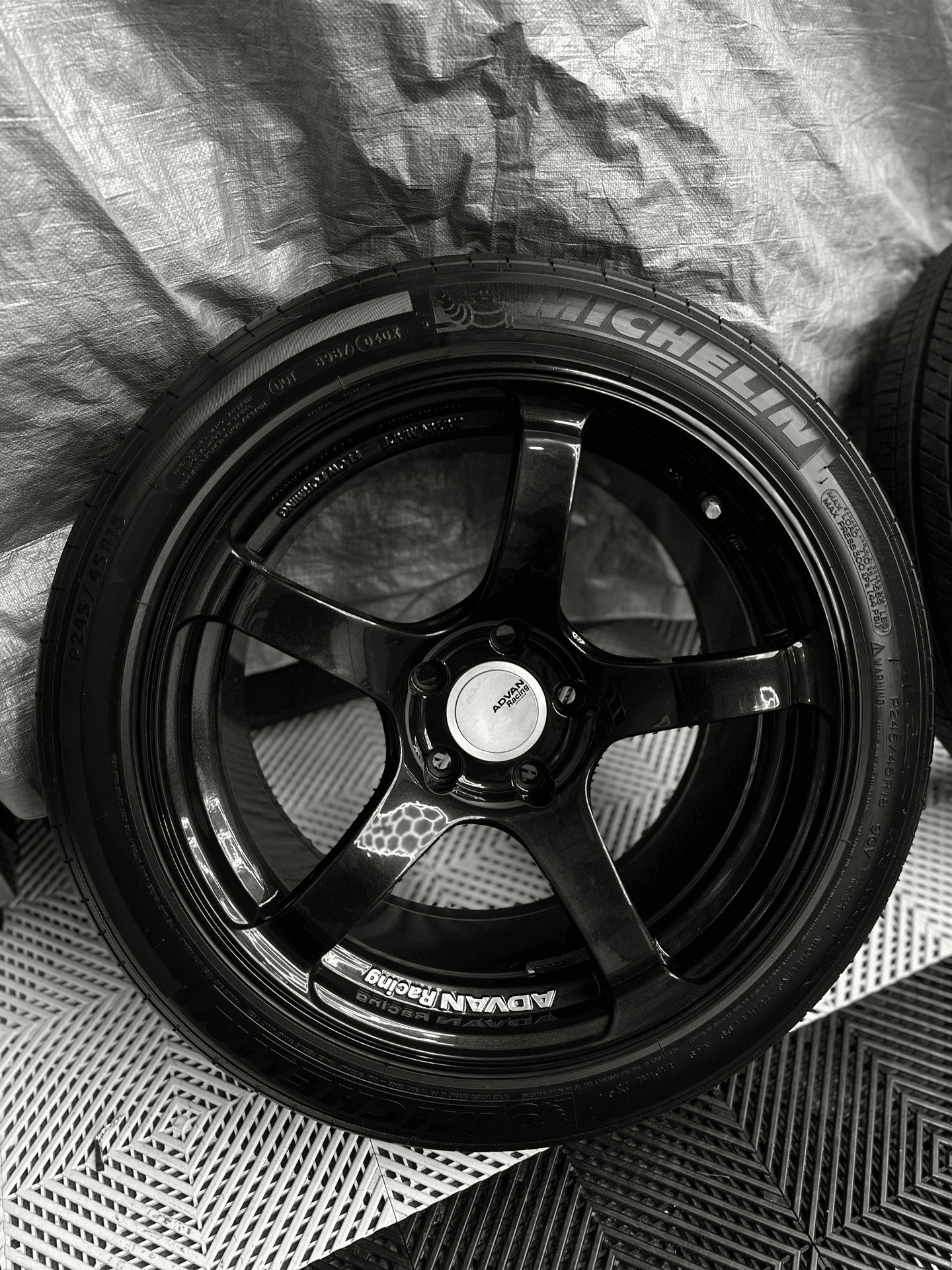 Black alloy wheel with Michelin and Advan Racing logos on a textured surface.